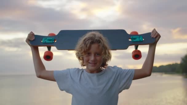 Силует, щасливий дитячий портрет молодого стильного ковзаняра, який тримає свій скейтборд на відкритому повітрі. — стокове відео