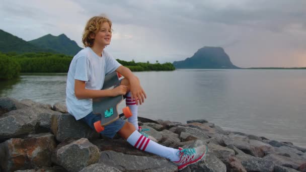 Garçon avec un longboard sur une belle plage. Adolescent skateboard sur fond coucher de soleil — Video