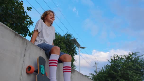Boldog tini, stílusos gördeszkás fiú fogja a gördeszkáját a szabadban — Stock videók