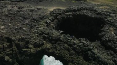 Dalgaların açık mavi sularla kayalık bir sahildeki hava görüntüleri.