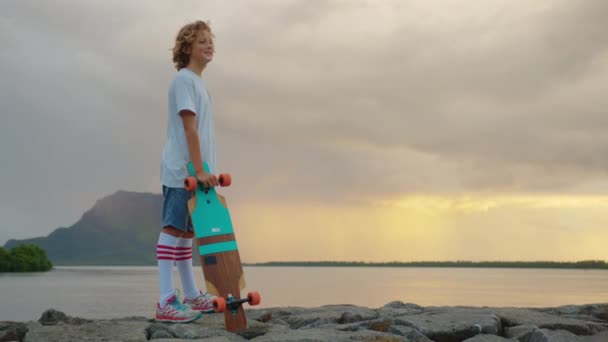Adolescente feliz, niño patinador elegante sosteniendo su monopatín al aire libre — Vídeos de Stock