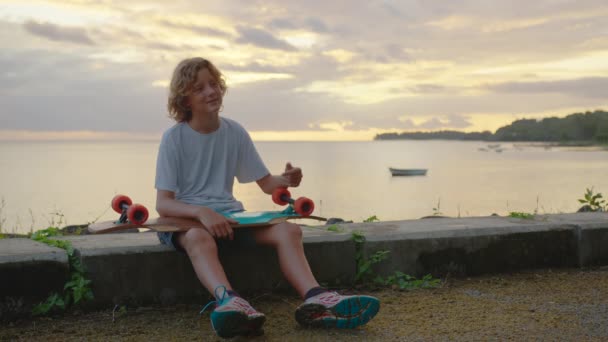 Silhouette, fröhliches Kinderporträt des jungen, stylischen Skater-Jungen mit seinem Skateboard im Freien — Stockvideo