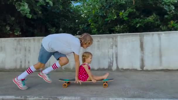 Una ragazzina cavalca su un longboard. Un bambino guida uno skateboard lungo una bella strada con palme. Intrattenimento e ricreazione concetto — Video Stock