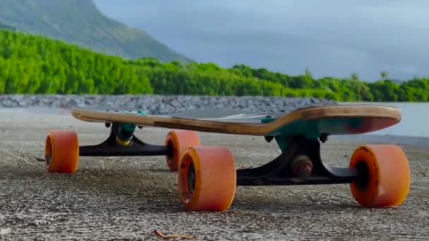 Um adolescente monta um longboard ao longo de uma bela estrada com palmeiras verdes — Vídeo de Stock