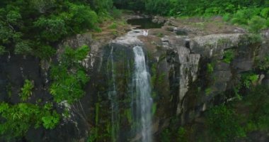Beyazlı kadın güzel şelalenin tepesinde kollarını kaldırıp Sunrise 'a bakıyor. Yeşil ormandaki yüksek şelalenin havadan görünüşü