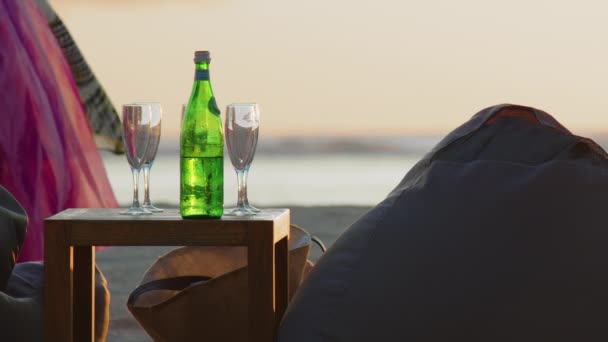 A bottle of water and glasses on a table against the background of the ocean. Sunset — Wideo stockowe