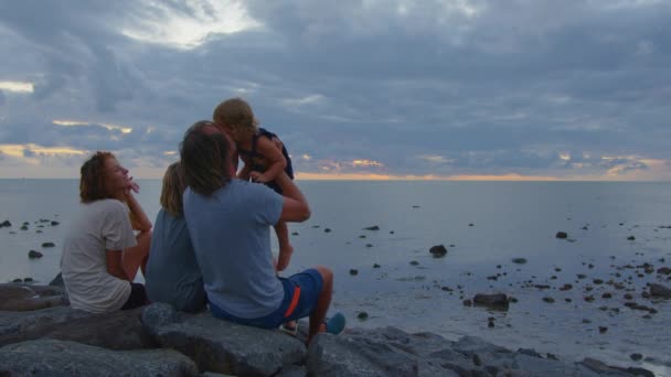 Szczęśliwa rodzina na plaży ogląda zachód słońca. Tata wymiotuje swoją córką. Dziecko uśmiecha się na tle pięknego nieba. — Wideo stockowe