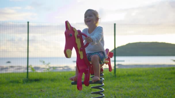 Baby rides on a horse swing on the playground. Happy family, child playing on a swing in the spring playground, childrens outdoor activities, life of little people on weekends, childrens dream — Vídeo de stock
