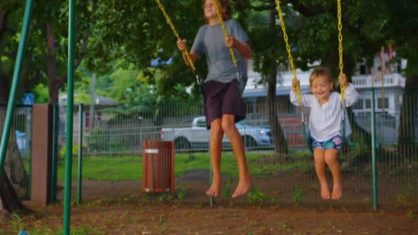 Fratello e sorella si stanno divertendo sull'altalena. Famiglia felice, bambino che gioca su un'altalena nel parco giochi primaverile, attività all'aperto per bambini, vita di piccole persone nei fine settimana, sogno dei bambini — Video Stock