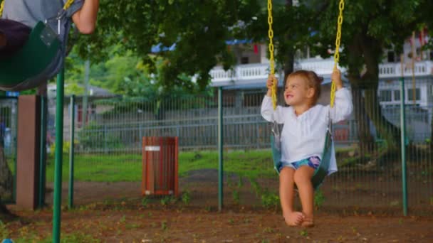 Brother and sister are having fun on the swing. The family is enjoying their leisure time. Family walk in the park — Stockvideo