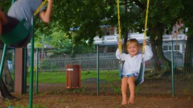 Brother and sister are having fun on the swing. A beautiful baby and a boy have fun spending their leisure time. Walk in the park
