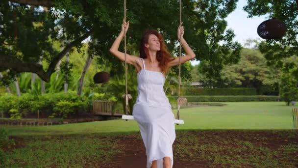 Ein Kindheitstraum vom Höhenflug auf einer Schaukel in einem grünen Wald. Ein junges Mädchen im weißen Kleid reitet auf einer Schaukel — Stockvideo