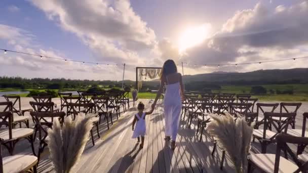 Malá dívka v bílých šatech drží ruku nevěsty ve svatebních šatech a jde na svatební oblouk na obřad — Stock video