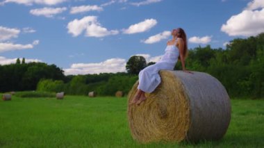 Attractive girl in a white dress on a green meadow enjoys freedom. Attractive brunette with curly hair lies on green grass in the sunset light. High quality 4k footage