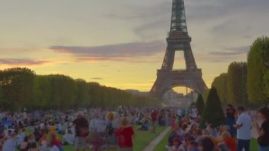 A timelapse of the Eiffel Tower along the river Seine. Eiffel Tower on Champs de Mars in Paris timelapse hyperlapse, France. Blue cloudy sky at summer day with green lawn and people walking around.