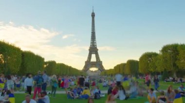 A timelapse of the Eiffel Tower along the river Seine. Eiffel Tower on Champs de Mars in Paris timelapse hyperlapse, France. Blue cloudy sky at summer day with green lawn and people walking around.