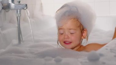 A little cheerful girl washes and plays in the bath with foam. Daily hygiene and skin care of children. Playing with water. Baby shampoo soap. High quality 4k footage