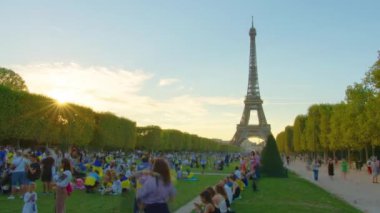 A timelapse of the Eiffel Tower along the river Seine. Eiffel Tower on Champs de Mars in Paris timelapse hyperlapse, France. Blue cloudy sky at summer day with green lawn and people walking around.
