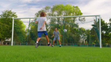 Ailenin parkta futbol oynarken çekilen yavaş çekim. Mutlu ebeveynler ve çocuklar yeşil çayırda topla oynuyorlar. Neşeli aile yazın dışarıda eğleniyor. Yüksek kalite 4k görüntü