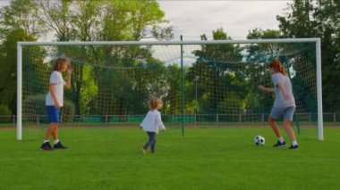 Ailenin parkta futbol oynarken çekilen yavaş çekim. Mutlu ebeveynler ve çocuklar yeşil çayırda topla oynuyorlar. Neşeli aile yazın dışarıda eğleniyor. Yüksek kalite 4k görüntü