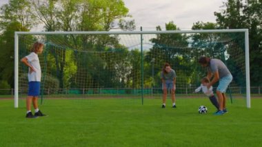 Baba, anne, oğul ve bebek parkta eğlenmek için futbol oynuyorlar. Mutlu bir aile. Ebeveynler ve çocuklar futbol oynuyor. Aile futbol topuyla çimenlikte. Çocuklar parkta birlikte top oynuyorlar..