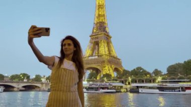 Fransa 'da yürüyen ve akıllı telefondan arkadaşlarıyla sohbet eden mutlu genç kadın turistlerin yavaş çekimleri. Eyfel Kulesi 'nin yanında kameranın önünde duran pozitif gezgin..