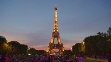 Eiffel Tower on Champs de Mars in Paris time lapse, France. Blue night cloudy sky at summer day with green lawn and people walking around. High quality 4k footage