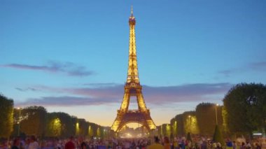 A timelapse of the Eiffel Tower along the river Seine. Eiffel Tower on Champs de Mars in Paris timelapse hyperlapse, France. Blue cloudy sky at summer day with green lawn and people walking around.