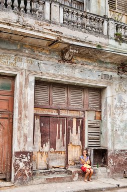 REGLA, CUBA - 22 Aralık 2019: Havana 'nın sakin mahallelerinden bazılarının tipik bir sahnesinde, isimsiz bir kadın eski bir dükkanın önünde sabırla oturur..