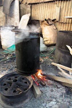 Güney Afrika Cape Town yakınlarındaki bir kasabada açık ateşte bir kuzu kafası çorbası pişiriliyor. Arka planda, teneke çarşaflar yemek pişirme alanını çevreleyen barakaların duvarlarını kaplıyor..