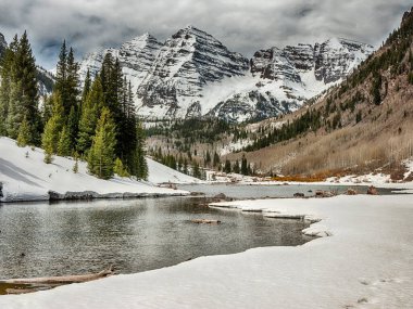 İlkbaharda olduğu gibi, arka planda Maroon Bells tepeleri olan, kardan akan akıntılarla dolu bir alp..