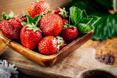 Tahta arka planda yaprakları olan taze sulu çilekler..