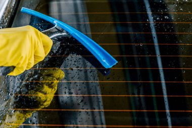 Bir adam arabayı yüksek basınçlı suyla yıkar ve fırçayla siler..