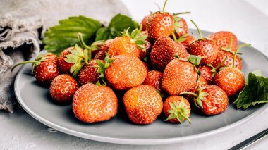 Beyaz beton arka planda yaprakları olan taze sulu çilekler..