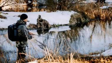 Elinde olta olan bir balıkçı baharın başlarında karla kaplı bir nehrin kıyısında balık yakalar..