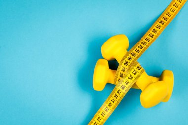 Sarı dambıllar ve ölçüm bandı mavi arkaplanda kopyalayacak bir yer