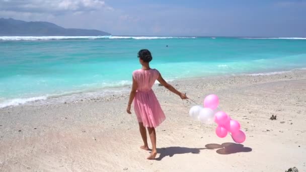 Encantadora dama en vestido rosa caminando con los globos hacia el océano, romántica celebrando en una isla tropical — Vídeo de stock