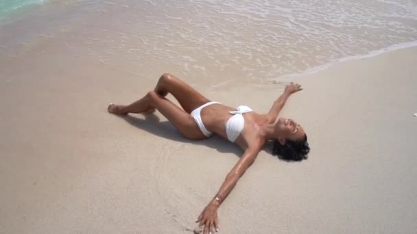 Oszałamiająca chuda kobieta w białym bikini leżąca na piasku, ciesząca się orzeźwiającymi falami oceanu, opalająca się — Wideo stockowe