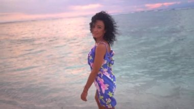 Deniz kıyısındaki güzel pembe gün batımında çıplak ayakla tatlı deniz suyunu deneyen mutlu kadın turist. 