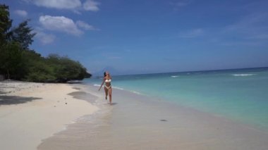 Kumlu sahil şeridinde bikinili, neşeli, egzotik bir tatil beldesinde koşan mutlu güzel kız. 