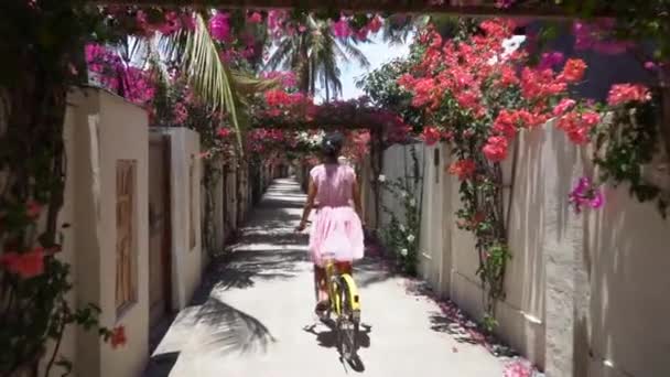 かわいいです女の子で美しいですドレス乗馬自転車雄大な熱帯壮大な通路でピンクの花 — ストック動画