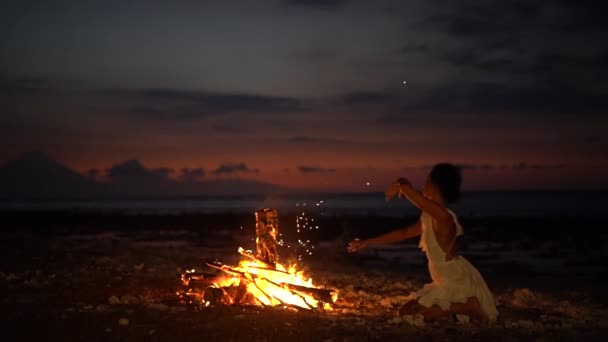 Mystisk kvinna dansar runt mysig öppen spis på stranden efter solnedgången, skymning festival händelse — Stockvideo