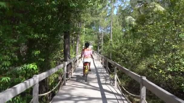 美しい熱帯の自然の中で田舎の木製の橋の上に自転車に乗るかわいい女の子のショットの後 — ストック動画