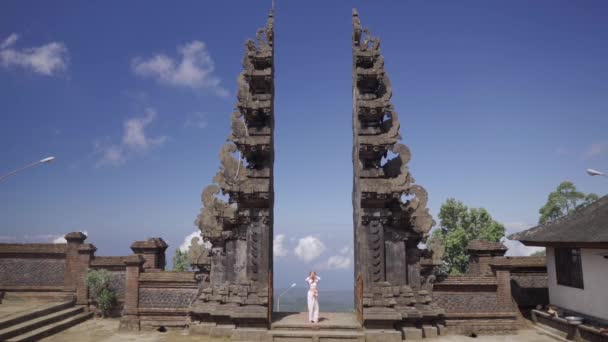 Femme en robe blanche priant, debout dans les célèbres portes de Bali, visite historique sacrée en Indonésie Vidéo De Stock Libre De Droits