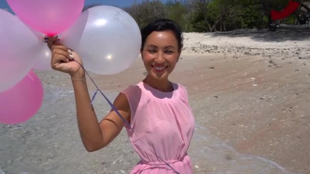 Romantikus születésnapi meglepetés az óceán partján, vidám nő rózsaszín ruhában, lufikkal a kezében, igazi boldogság. — Stock videók