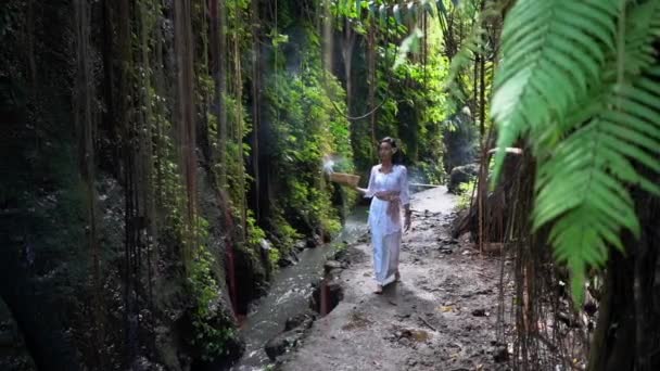Gudomlig kvinna går i den tropiska djungeln längs bäcken, mediterar kontemplation, brännande rökelser — Stockvideo