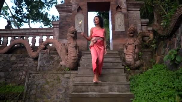 Prachtige vrouw die de trap afloopt van een heilige boeddhistische tempel, brandende ceremoniële wierookstokjes — Stockvideo