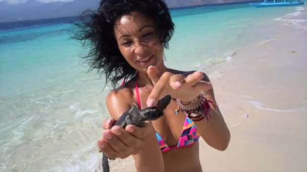 Wesoła kobieta trzymająca małego żółwia w rękach, pokazująca do kamery słodkie stworzenie oceanu, fale na tropikalnej plaży — Wideo stockowe