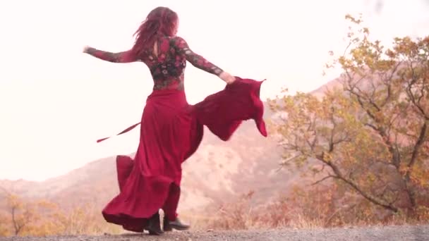Csodálatos vörös hajú mágikus nő táncol egy hosszú piros szoknya szélén a hegyek arany erdő — Stock videók