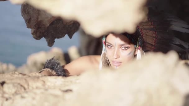 Retrato de modelo de mujer asombrosa con maquillaje colorido y vestido y sombrero indio americano en las rocas — Vídeos de Stock